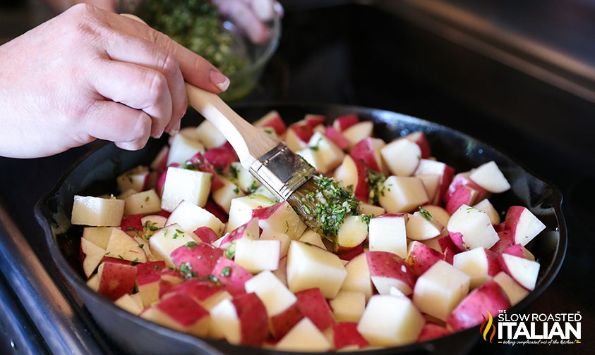 brushing olive oil mixture over potatoes in skillet