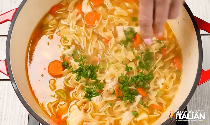 adding fresh parsley to pot of chicken noodle soup