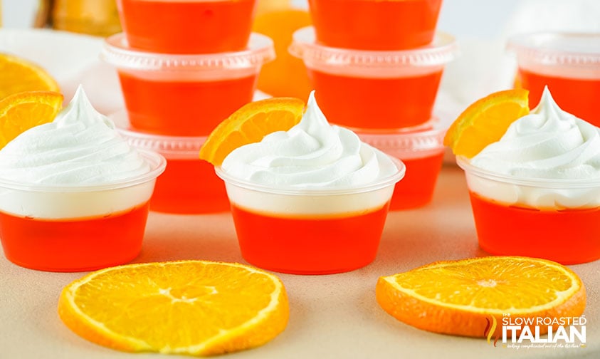 orange jello shots with whipped cream, more stacked in background