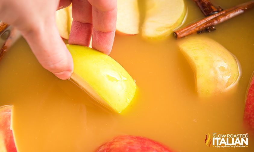 adding apple slices to pot of cider