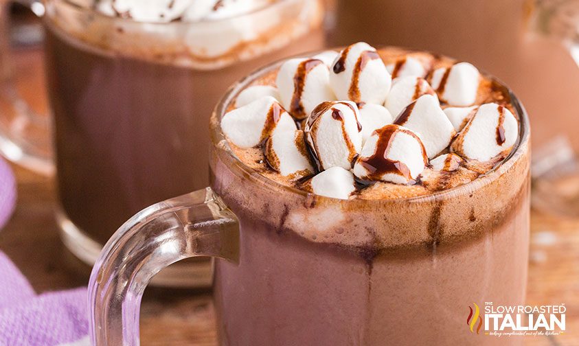 close up: clear mug of hot chocolate topped with marshmallows and chocolate sauce