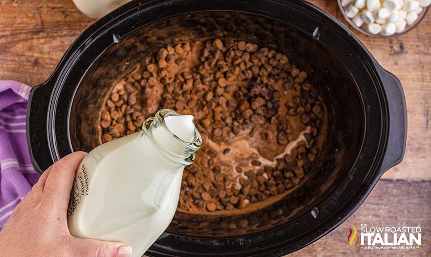 pouring milk over cocoa powder and chocolate chips in crockpot