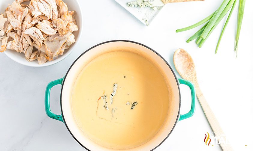 overhead: pot of buffalo cheese sauce next to a bowl of shredded chicken