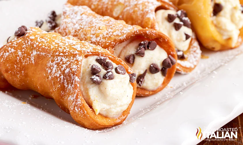 row of homemade cannoli with mini chocolate chips dusted with powdered sugar