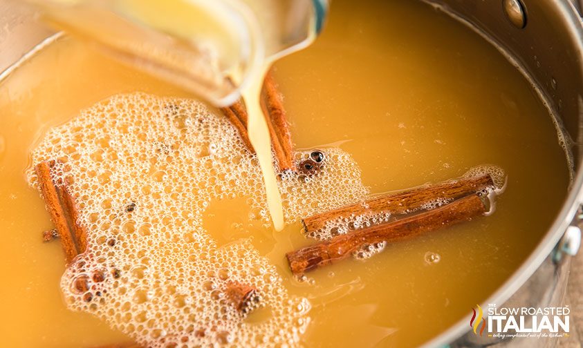 pouring cider into pot with cinnamon sticks