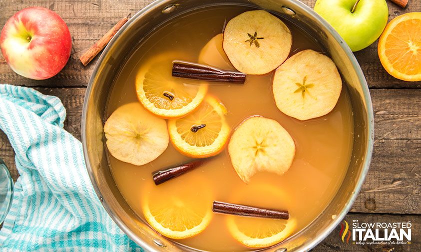 apple and orange slices floating in pot of cider with cinnamon sticks
