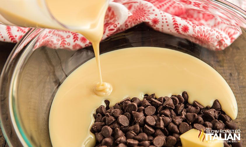 pouring sweetened condensed milk into bowl with butter and chocolate chips