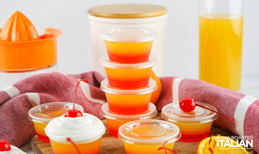 stacked tequila sunrise jello shots, one with whipped cream and a cherry