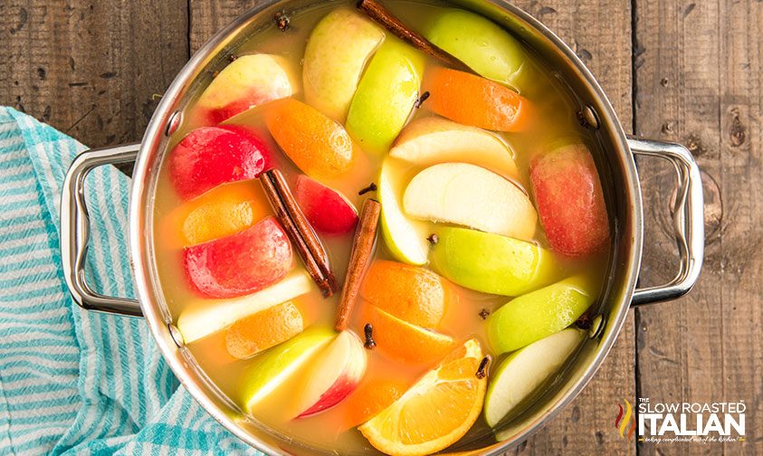 overhead: pot of cider with apple and orange slices, cinnamon sticks, and cloves