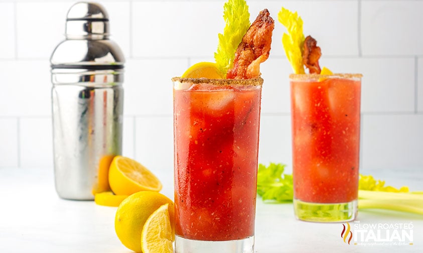 two glasses of bloody mary drink garnished with bacon and celery
