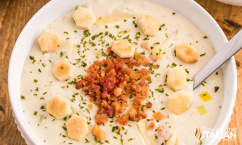 bowl of clam chowder topped with oyster crackers, bacon crumbles, and herbs