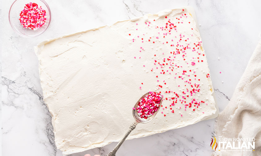 adding icing and sprinkles to red velvet poke cake