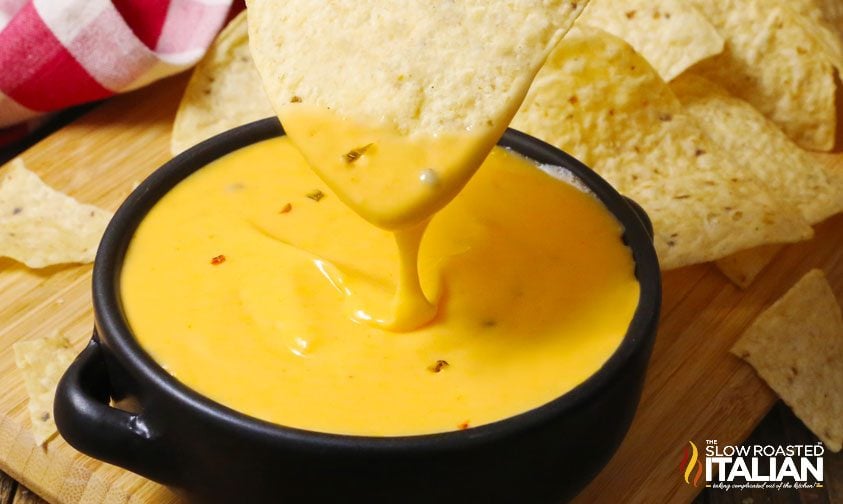 dipping tortilla chips in bowl of cheese sauce