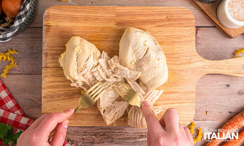 shredding chicken breasts on a wood cutting board
