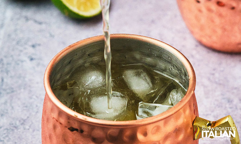 adding ginger beer to whiskey in copper mug