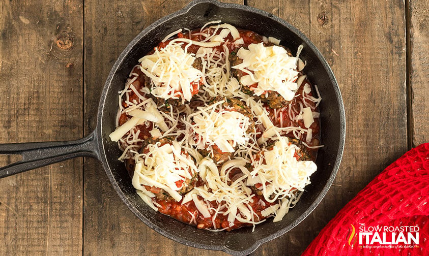 shredded cheese placed on meatballs in a skillet