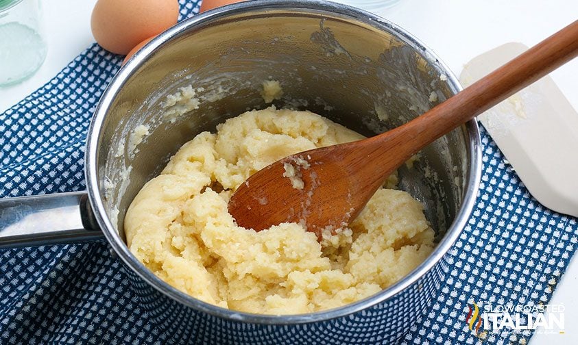 mixing churro dough in saucepan with wooden spoon