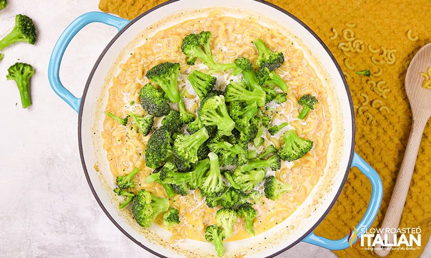 adding frozen broccoli to pot of macaroni and cheese