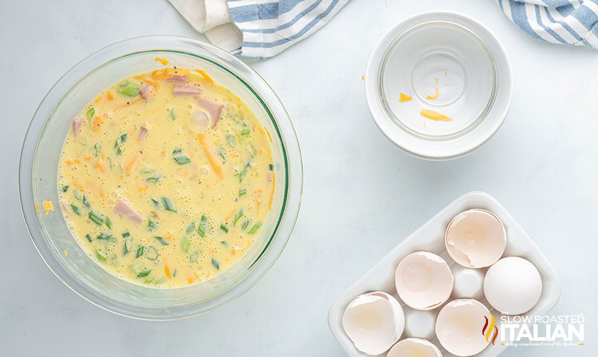 quiche filling in a bowl, empty bowls and cracked eggs nearby