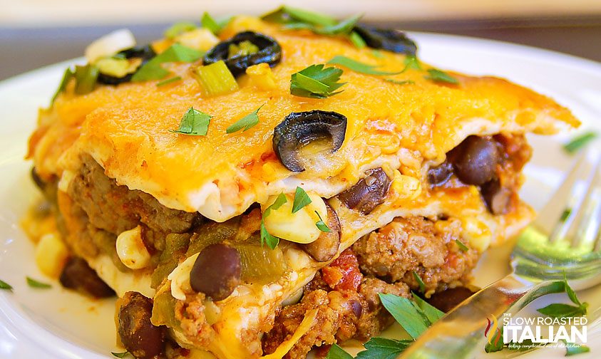 close up: slice of taco lasagna topped with olives and cilantro