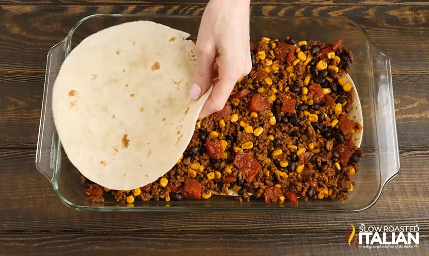 adding a layer of tortillas over ground beef mixture in baking dish