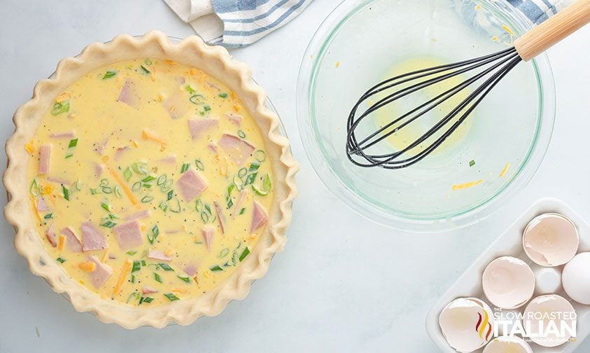 quiche filling in pie crust, empty bowl with whisk nearby