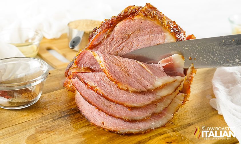slicing maple glazed ham on wooden surface