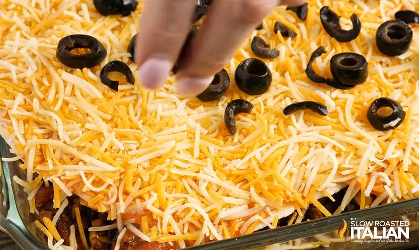 close up: sprinkling sliced olives over shredded cheese on mexican lasagna