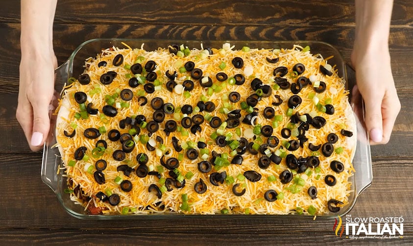 mexican lasagna in baking dish topped with olives and green onions