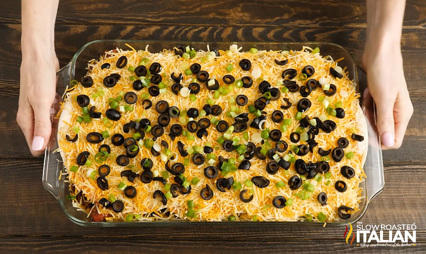 mexican lasagna in baking dish topped with olives and green onions