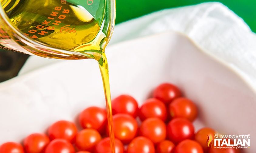 pouring olive oil over cherry tomatoes in baking dish