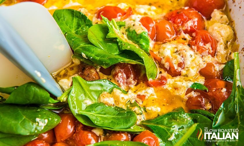mashing spinach leaves into crushed tomato and feta sauce