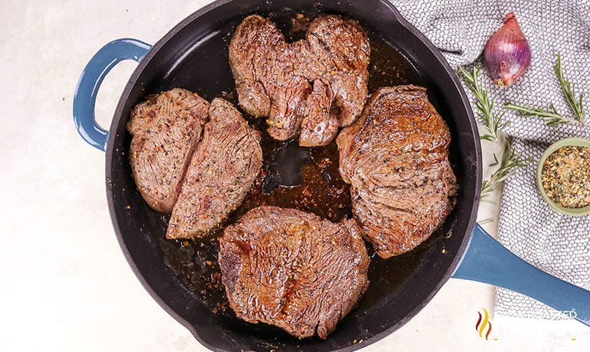 seared steaks in skillet with red wine sauce