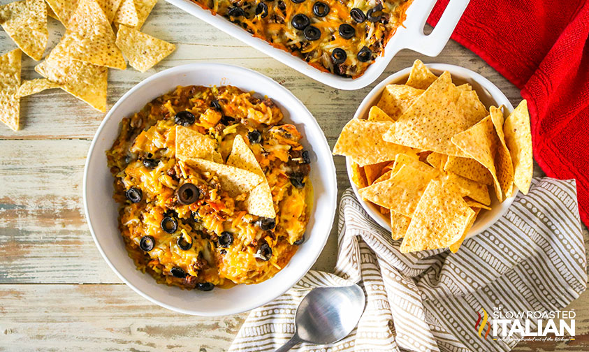 7 layer bean dip in a bowl with tortilla chips scattered