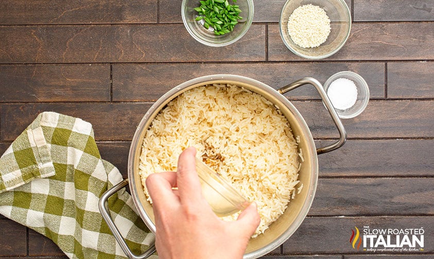 adding toasted sesame oil to pot full of cooked rice