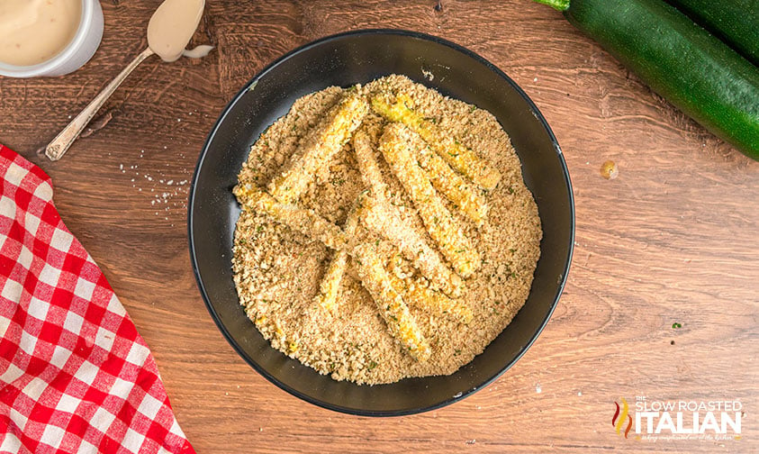 pressing zucchini sticks in breadcrumbs