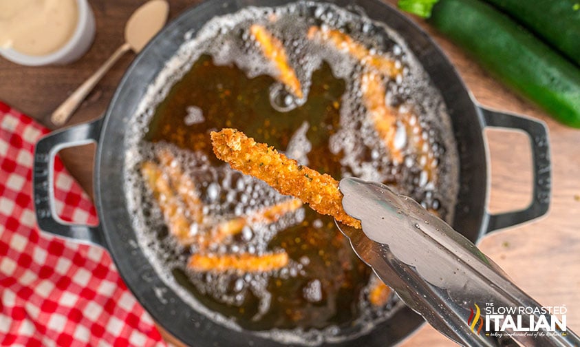 tongs holding a fried zucchini stick