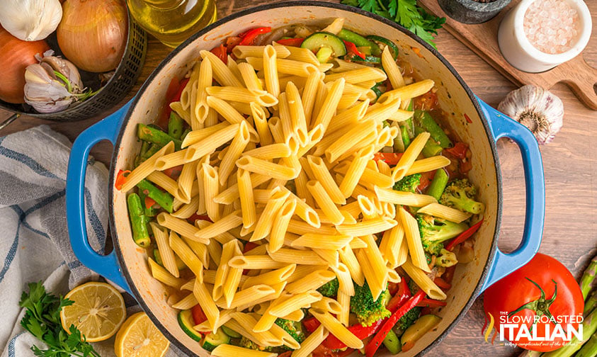 cooked penne pasta added to vegetables in a dutch oven