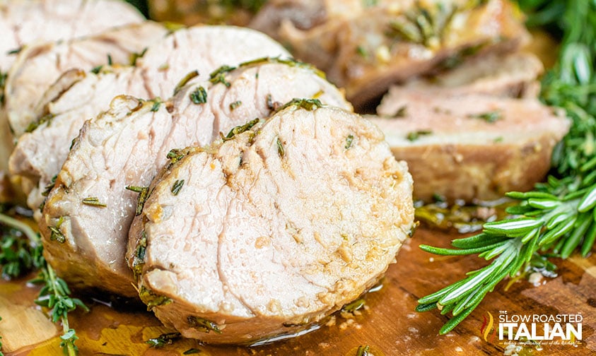 sliced herb roasted pork tenderloin on a cutting board with sprigs of rosemary