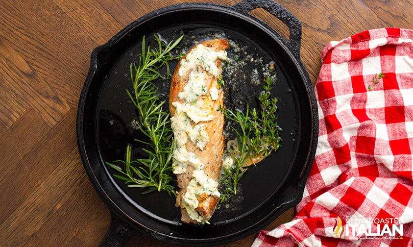 adding herb butter to pork tenderloin in a cast iron skillet