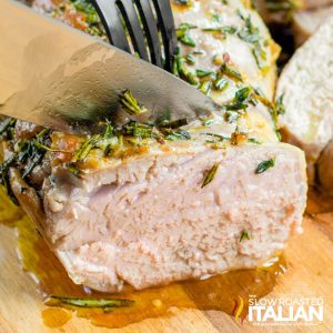 slicing herb roasted pork tenderloin on a wood cutting board