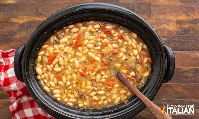 crockpot full of italian beans with a wooden spoon