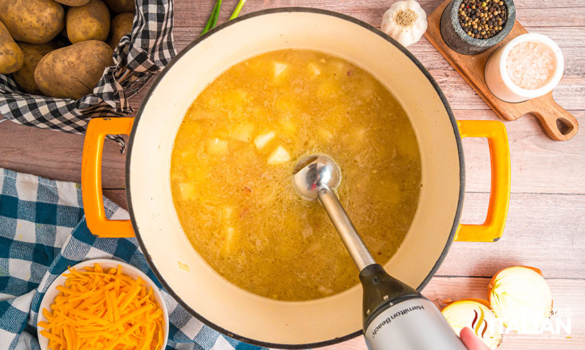 using an immersion blender to mash potatoes in baked potato soup