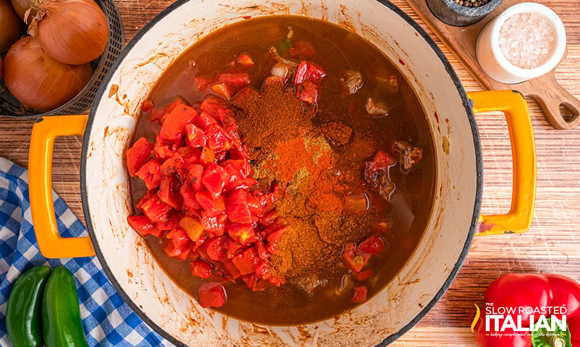 adding tomatoes and spices, and beef stock to large pot