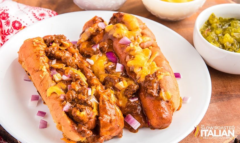 plate with two chili dogs topped with cheese and red onion