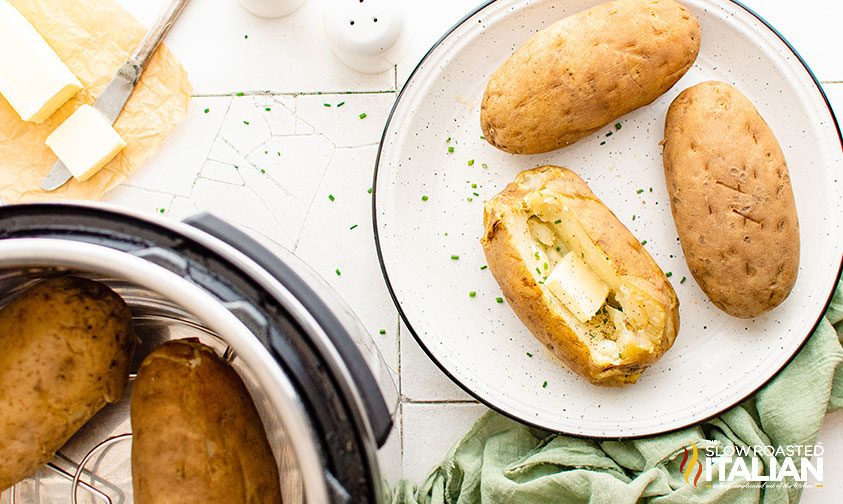 baked potatoes on plate, one sliced open with butter and chives