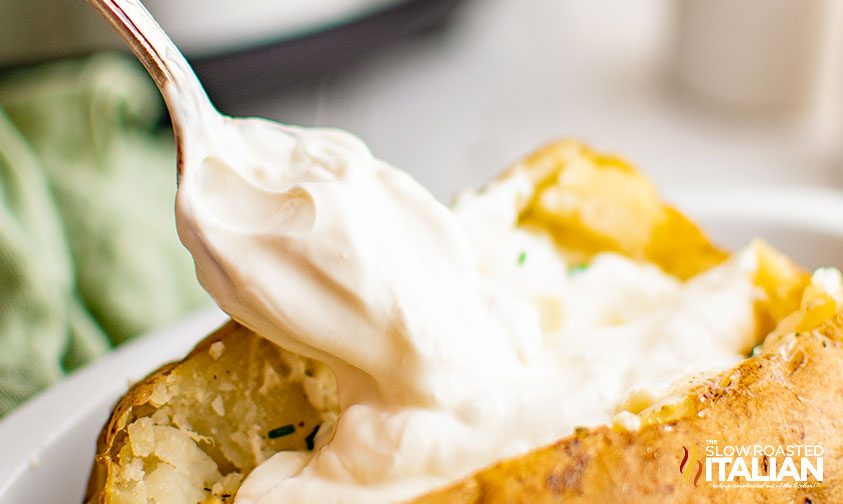 spooning sour cream onto baked potato