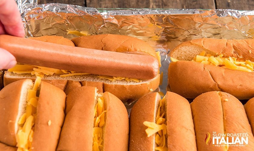 placing hot dog in bun with shredded cheese