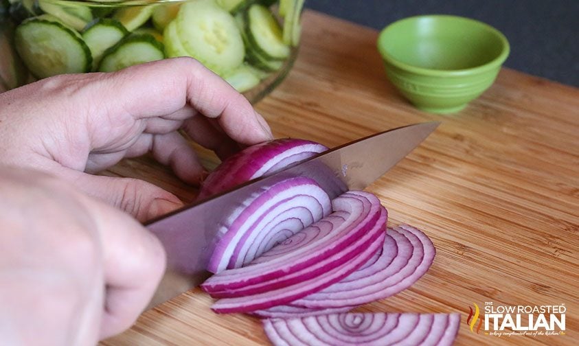 slicing red onion with bowl of cucumber slices in background