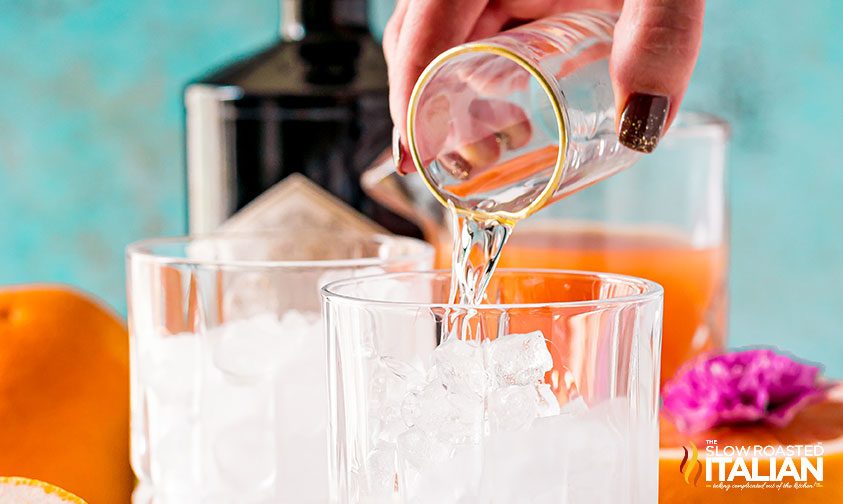 pouring gin over ice in rocks glass